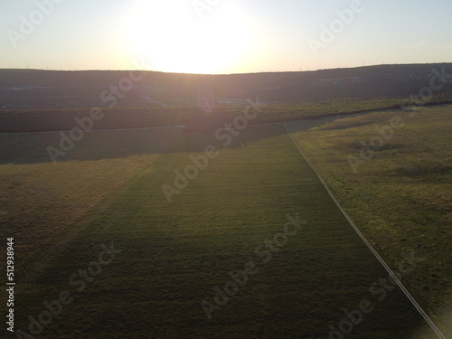 Aerial view on green wheat field in countryside. Field of wheat blowing in the wind on sunset. Young and green Spikelets. Ears of barley crop in nature. Agronomy, industry and food production.