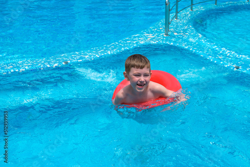 Little boy of 7 years swimming in pool with inflatable rubber ring. Funny happy child playing in aquapark. Summer holidays and vacation, travel and tourism concept. © Elena