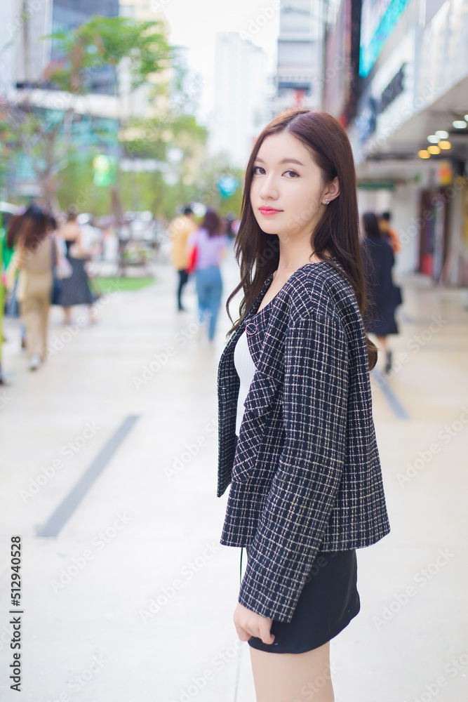 Portrait of a beautiful, long-haired Asian female in a black pattern coat with braces on teeth walking and smiling outdoors in the city.