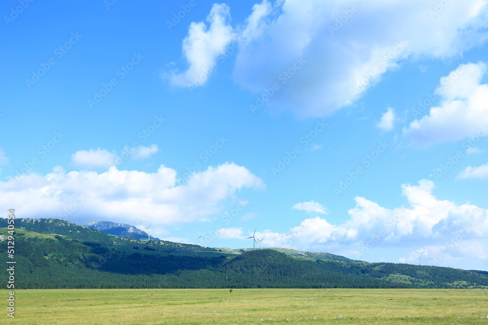 Mountain landscape with meadows, hills and beautiful blue sky with some clouds. Windmills in background.