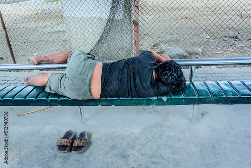 A homeless man with black T-shirt sleeping on a bus stop bench. Can used for concepts of homelessness , madman , drunker and other. photo