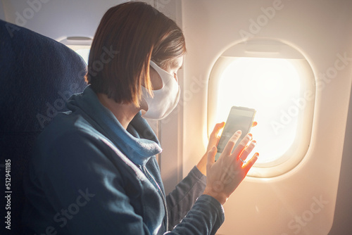 Young beautiful woman sitting at window of plane during the flight. new normal travel after covid-19 pandemic concept. taking photo from an airplane window