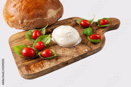 Cherry tomato oo basil leaf, mozzarella on wooden kitchen board, bread on white.