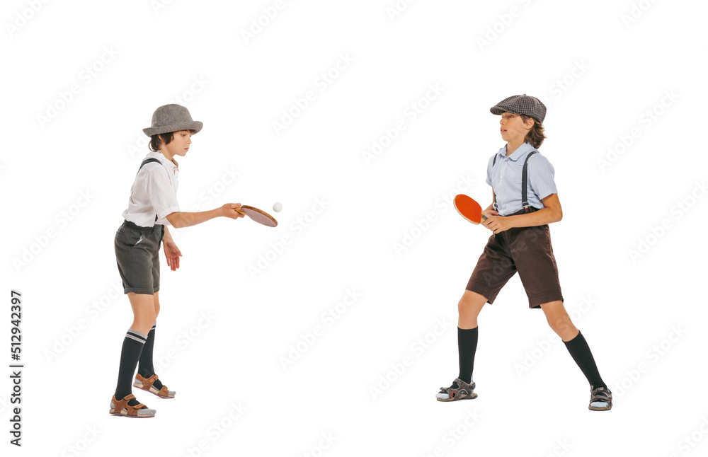 Two school age boys, stylish kids wearing retro clothes playing ping-pong isolated over white background. Concept of childhood, hobby