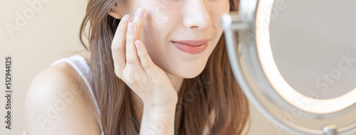 Fresh healthy skin, beautiful asian young woman, girl looking at mirror, applying moisturizer on her face, hand in putting cream treatment before make up cosmetic routine at home. Facial Beauty.