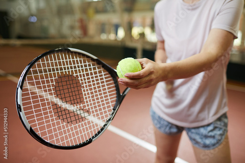 Close-up of unrecognizable woman in loose tshirt standing on indoors court and holding green ball while preparing for serving tennis ball © Mediaphotos