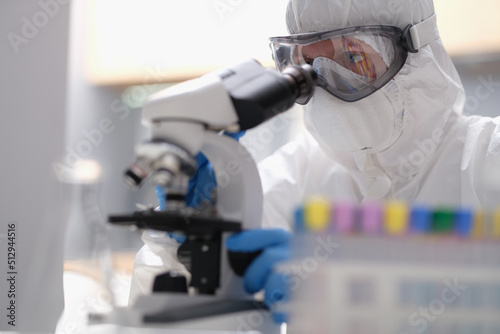 Scientist in a protective suit looking through a microscope in modern equipped laboratory