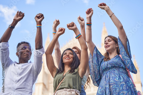 Group of multiracial people standing together outdoors while raising hands with LGBT rainbow flag wristbands. Diversity, equality and unity concept.