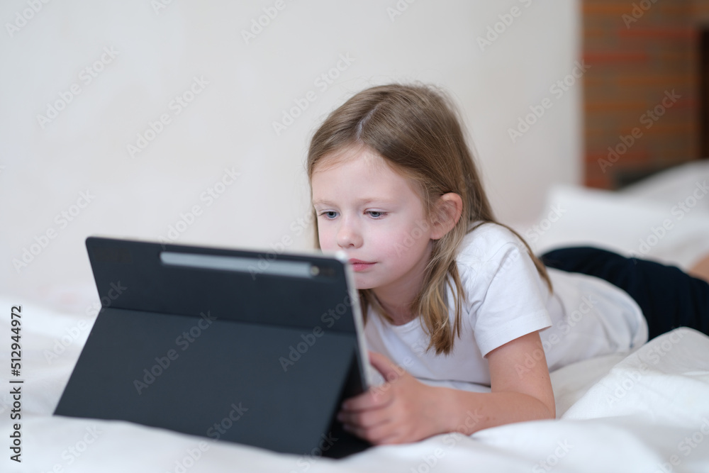 Little girl carefully looks at tablet while lying on bed Little girl carefully looks at tablet while lying on bed