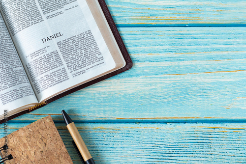 Daniel open Holy Bible Book on a rustic wooden table background with a notebook and pen. Copy space. Studying old Testament prophecy, Christian biblical concept. Top view. Flat lay. 