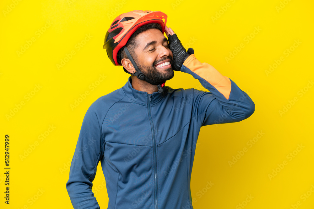 Young cyclist Brazilian man isolated on yellow background smiling a lot Young cyclist Brazilian man isolated on yellow background smiling a lot