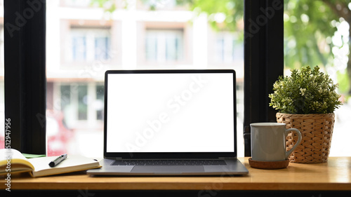 Front view laptop computer, coffee cup, houseplant and notebook on white table. Comfortable workplace