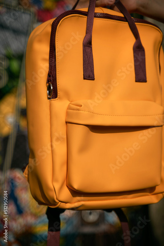 Solid yellow color backpack mockup. Hand holds a no logo colorful backpack template. Concept of young people traveling.