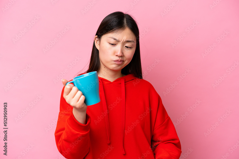 Young Chinese woman holding cup of coffee isolated on pink background with sad expression Young Chinese woman holding cup of coffee isolated on pink background with sad expression