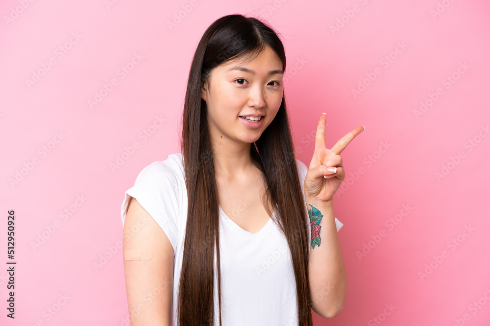 Young Chinese woman wearing a band aids isolated on pink background smiling and showing victory sign Young Chinese woman wearing a band aids isolated on pink background smiling and showing victory sign