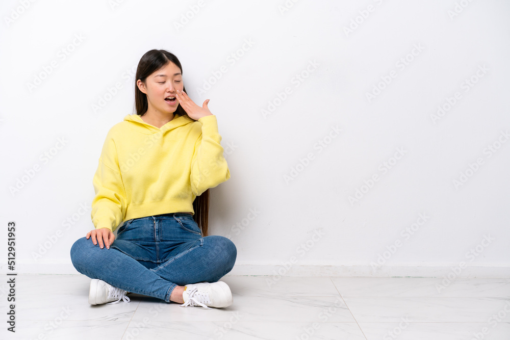 Young Chinese woman sitting on the floor isolated on white wall yawning and covering wide open mouth with hand Young Chinese woman sitting on the floor isolated on white wall yawning and covering wide open mouth with hand
