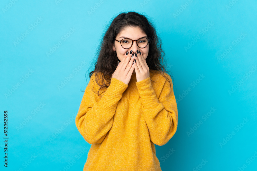 Teenager Russian girl isolated on blue background happy and smiling covering mouth with hands Teenager Russian girl isolated on blue background happy and smiling covering mouth with hands