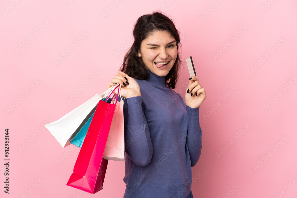 Teenager Russian girl isolated on pink background holding shopping bags and a credit card