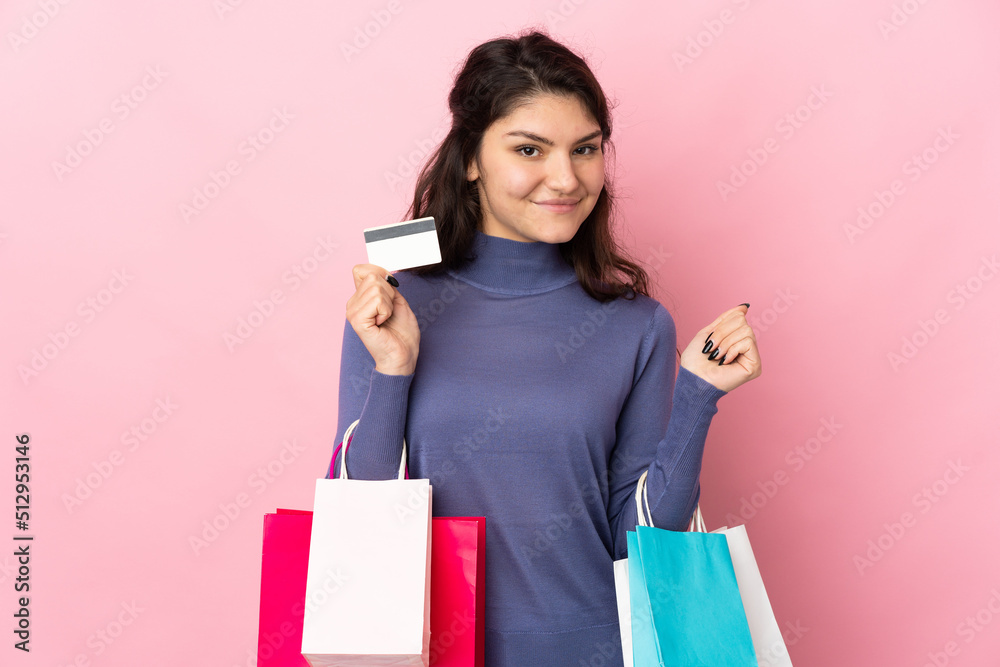 Teenager Russian girl isolated on pink background holding shopping bags and a credit card Teenager Russian girl isolated on pink background holding shopping bags and a credit card