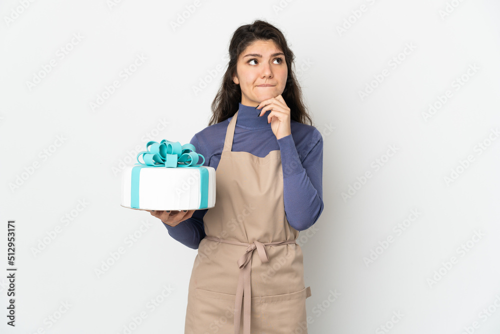 Pastry Russian chef holding a big cake isolated on white background having doubts and thinking Pastry Russian chef holding a big cake isolated on white background having doubts and thinking