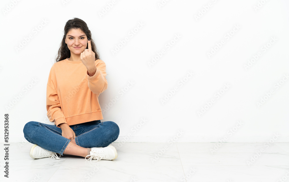 Teenager Russian girl sitting on the floor doing coming gesture Teenager Russian girl sitting on the floor doing coming gesture