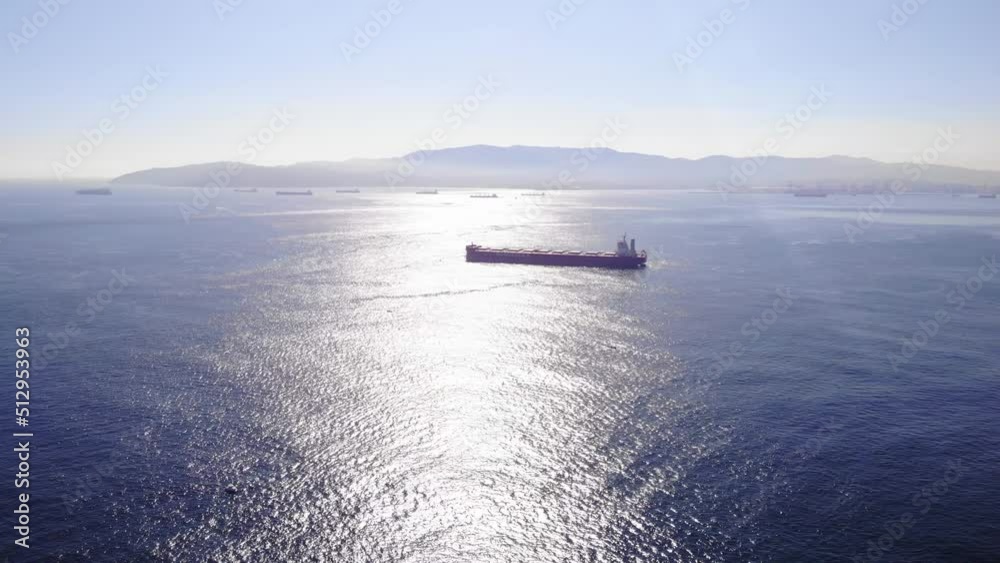Aerial View Of Cargo Ship Travelling Through The Strait Of Gibraltar With Sunshine Reflected On Waters Surface. Dolly Forward Aerial View Of Cargo Ship Travelling Through The Strait Of Gibraltar With Sunshine Reflected On Waters Surface. Dolly Forward