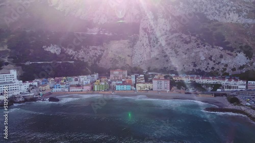 Aerial View Of Waves Breaking At Catalan Bay With Colourful Buildings On Beachfront With Sun Flares In View. Circle Dolly