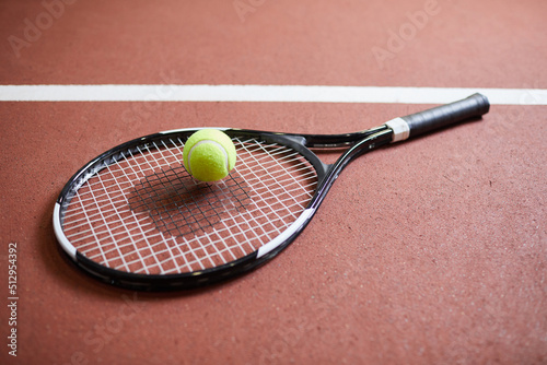 Close-up of tennis player equipment such as racket and ball placed on red stadium floor, tennis game concept © Mediaphotos