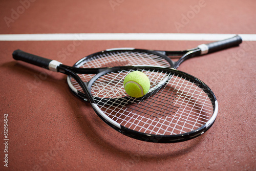 Close-up of professional equipment for tennis lying on red floor: rackets with ball stacking on court © Mediaphotos