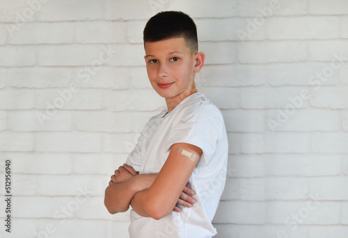 teenager in a white t-shirt with a medical plaster on his arm after vaccination or inoculation, medicine and prevention of childhood diseases