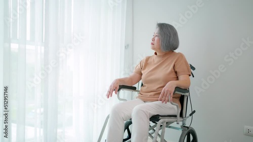 Elderly woman sitting on the wheelchair and looking outside windows. Young pretty caregiver touch elderly woman hand encourage. Older woman feeling happy and smile. Healthcare and therapy.