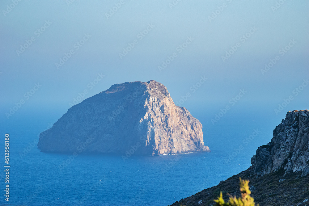 Naklejka premium The magical islet of Hytra or else Avgo (Egg) close to Kapsali, Kythera idland. The steep and rocky inhospitable territory is decorated by the yellowish semprevivum, and is also a nesting falcon place