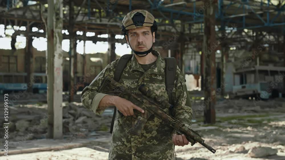 Portrait of patriot soldier in military uniform and protective helmet holding gun in hands while standing on abandoned plant. Caucasian brave man looking at camera with confidence in eyes. Portrait of patriot soldier in military uniform and protective helmet holding gun in hands while standing on abandoned plant. Caucasian brave man looking at camera with confidence in eyes.