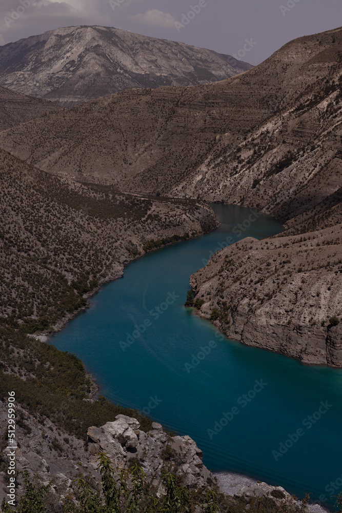 Obraz premium Majestic colorful turquoise blue river and high steep mountain slopes of canyon, clear sky, vertical. Mountain landscape. Hiking, tourism, travel in wild outdoor of Dagestan Caucasian ridges.