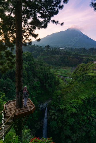 A waterfall on a cliff and surrounded by trees with Merapi Volcano on the background in the morning. Kedung Kayang waterfall, Indonesia photo