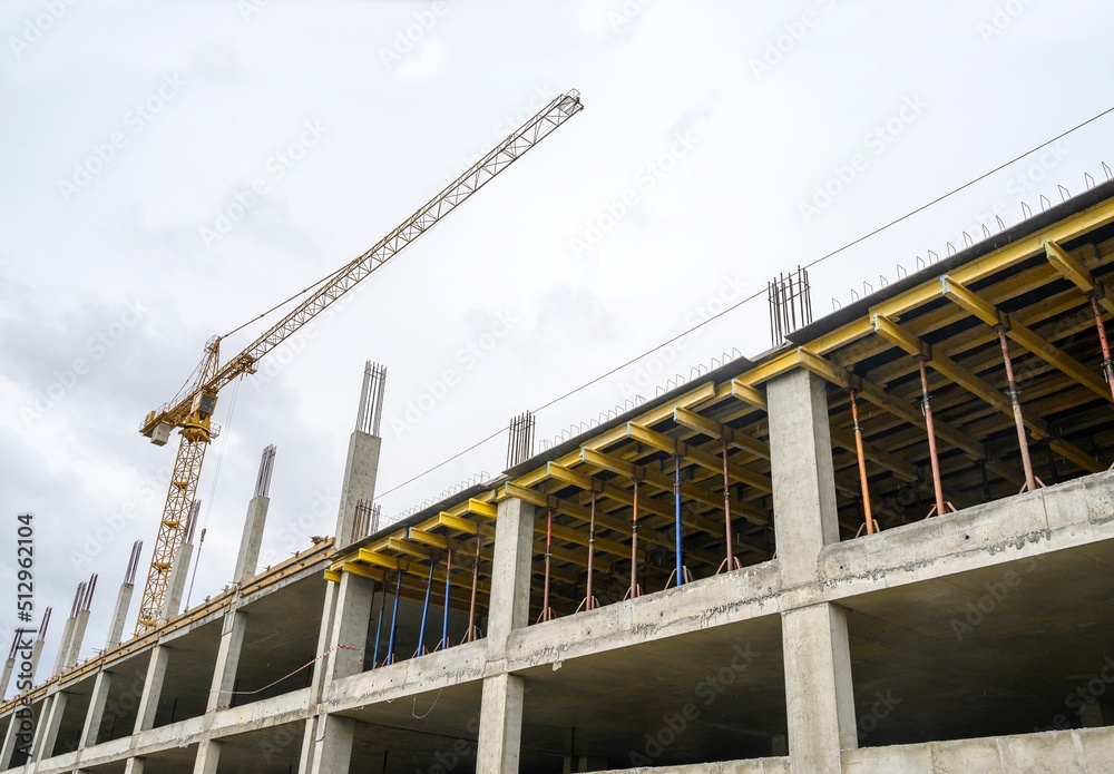  One construction crane while working at a construction site in cloudy spring weather against the backdrop of a blue sky, with clouds and multi-storey buildings. No people street photo.