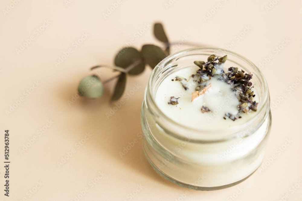 Handmade candle from paraffin and soy wax in glass with wooden wick and dry herbal isolated on pastel beige background. Flat lay, top view, copy space