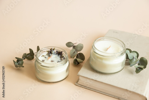 Canvastavla Two candmade candles from paraffin and soy wax in glass with wooden wick and dry herbal isolated on pastel beige background