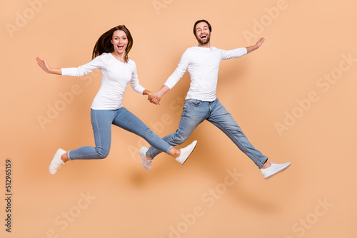 Full length body size view of two attractive cheerful partners jumping running isolated over beige pastel color background