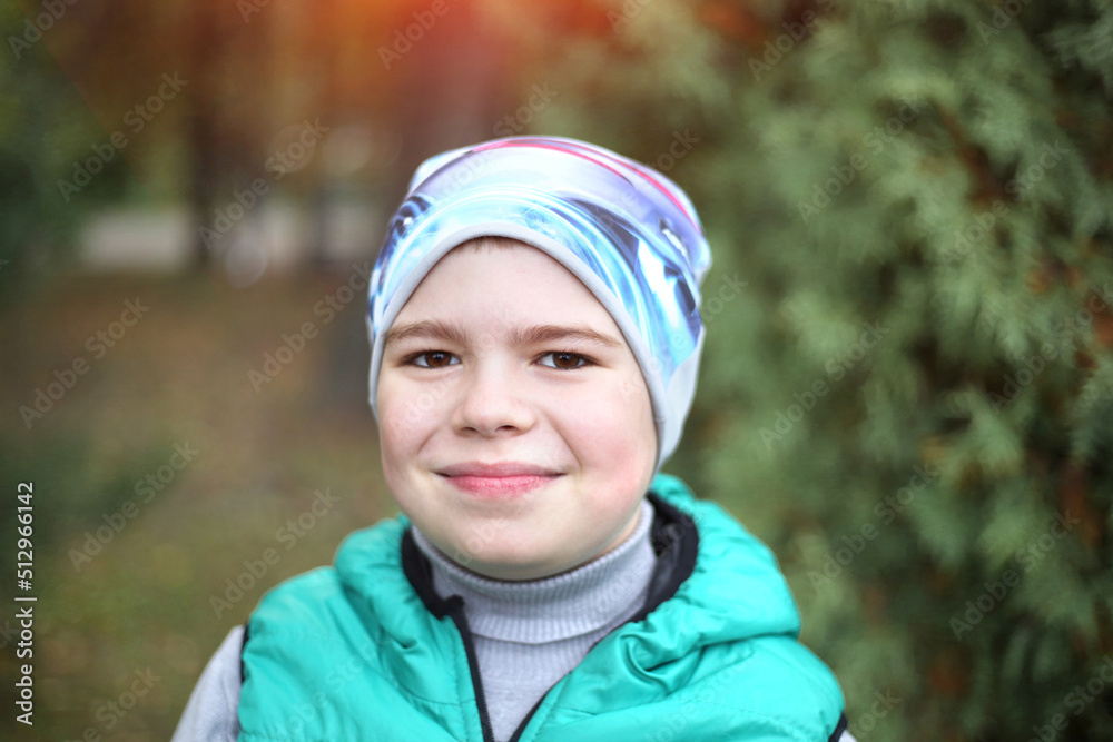 Cute Caucasian teenager boy smiling looking at the camera, wearing a hat and a green vest. Autumn park background. Relaxation. Childhood concept Cute Caucasian teenager boy smiling looking at the camera, wearing a hat and a green vest. Autumn park background. Relaxation. Childhood concept