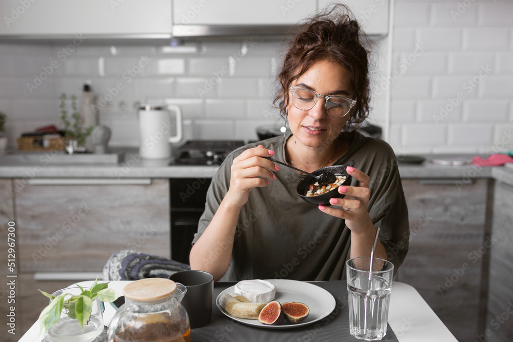 beautiful girl in glasses with curly hair eating breakfast on the kitchen , early morning mood, morning snacks, healthy life, healthy food, healthy breakfast