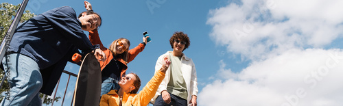 Φωτογραφία low angle view of happy women showing success gesture near interracial skaters, banner