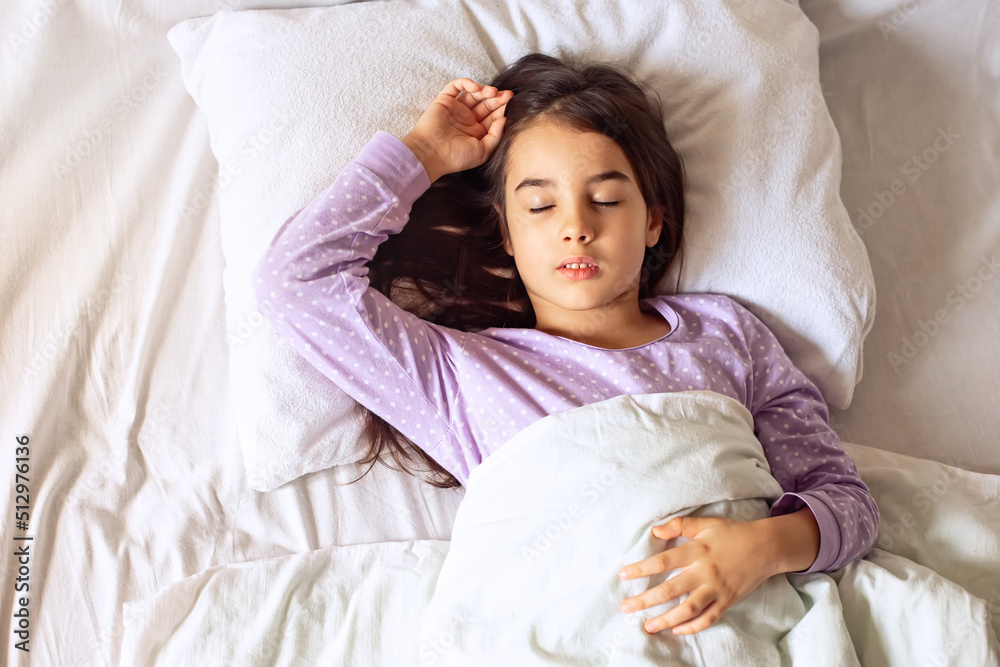 Little brunette girl sleeps lying on a white pillow on the bed. Little brunette girl sleeps lying on a white pillow on the bed.