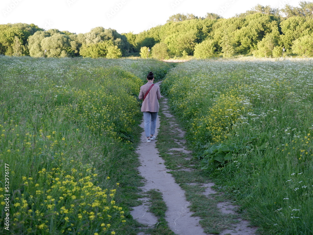 A girl walks along a path in the middle of a luxuriously blooming meadow. A girl walks along a path in the middle of a luxuriously blooming meadow.