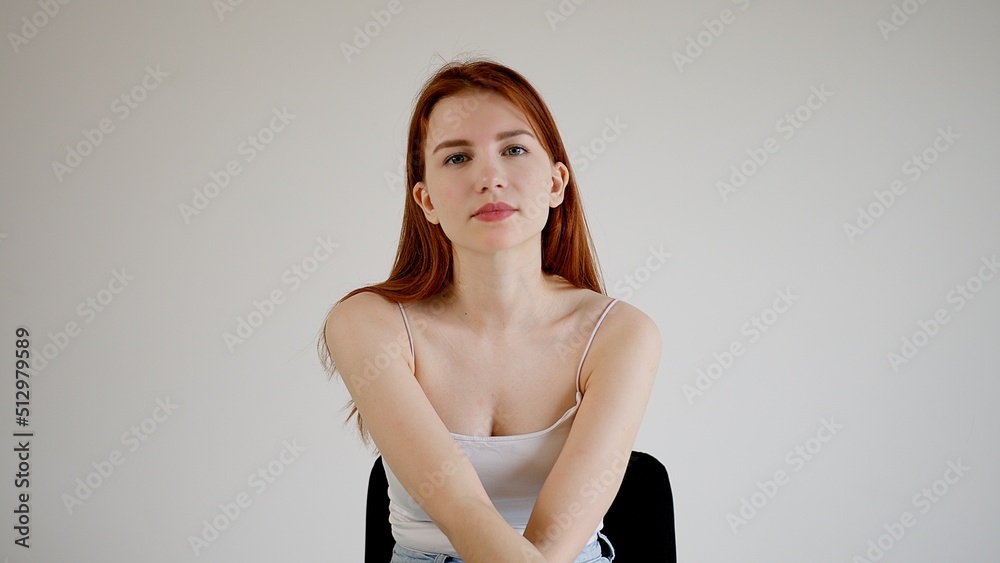 Fototapeta premium Beautiful red-haired young attractive woman sits on a chair