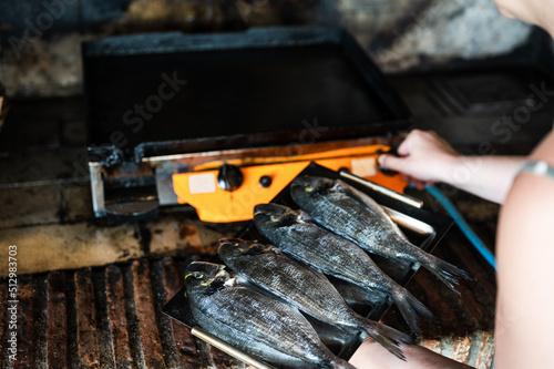Woman holding fresh fish (Gilt-head bream) ready to be prepared on gas griddle plate stove.Goldfish, Sparidae