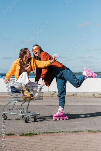 thrilled woman riding rollers skates near friend in shopping cart.