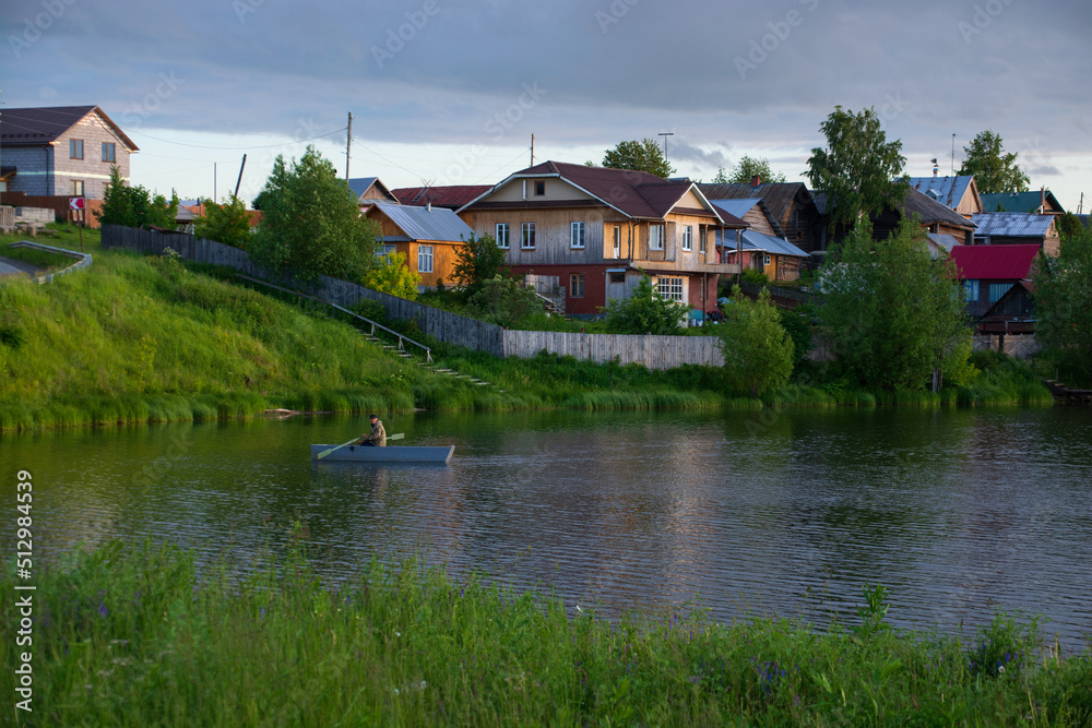 a village on the river bank with bright green grass and a beautiful sky.