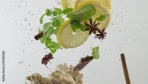 Citrus lemonade with spices. Fresh yellow lemon, ginger, mint, cinnamon, star anise falling into water with bubbles and floating in cold water slow motion close-up photo