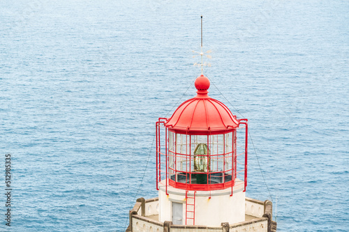 The top of the lighthouse is red color with a weather vane at the top, against the background of sea water